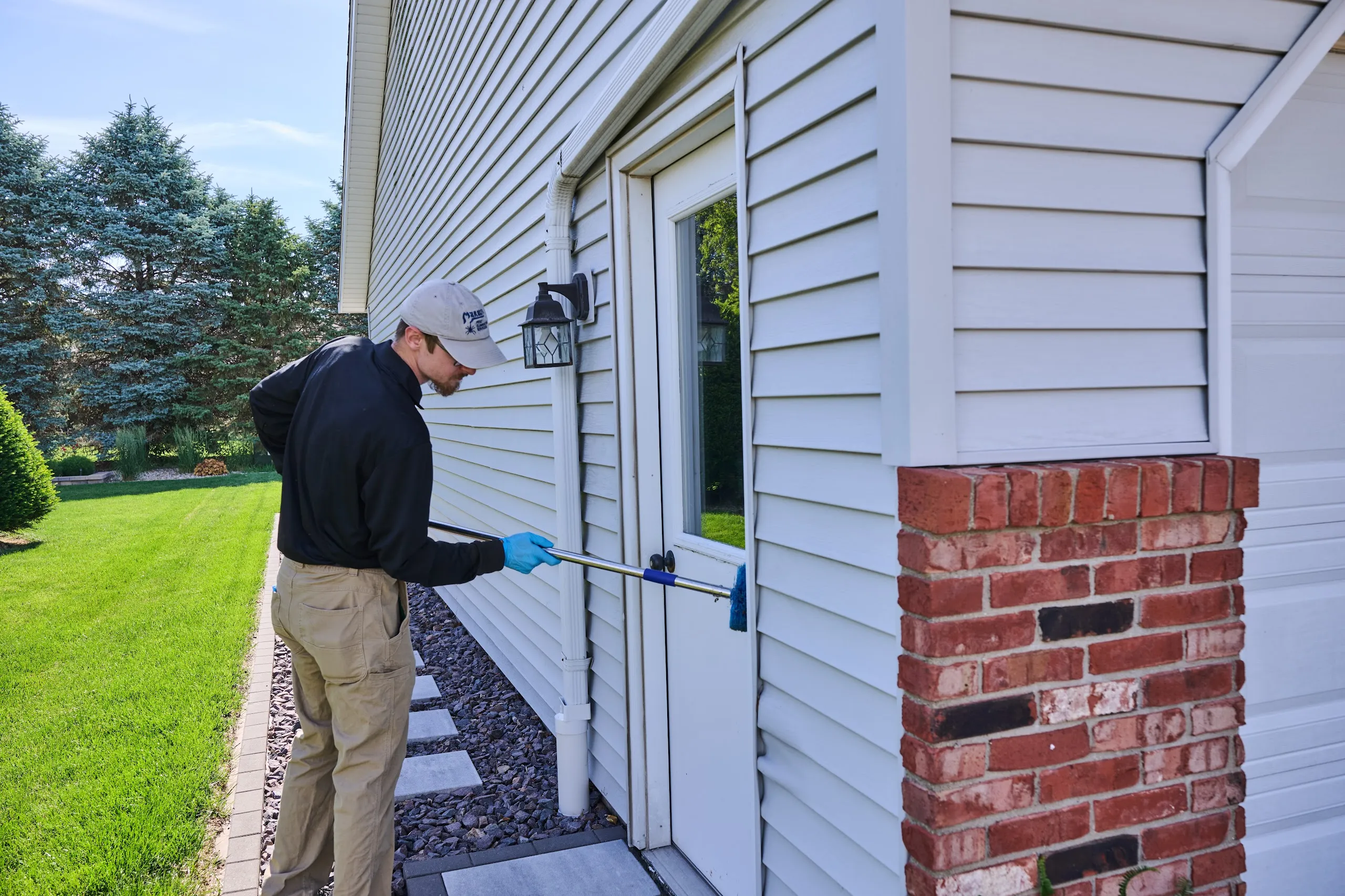 A Markley's technician in gloves applying a treatment around the side entry door and foundation of a home.